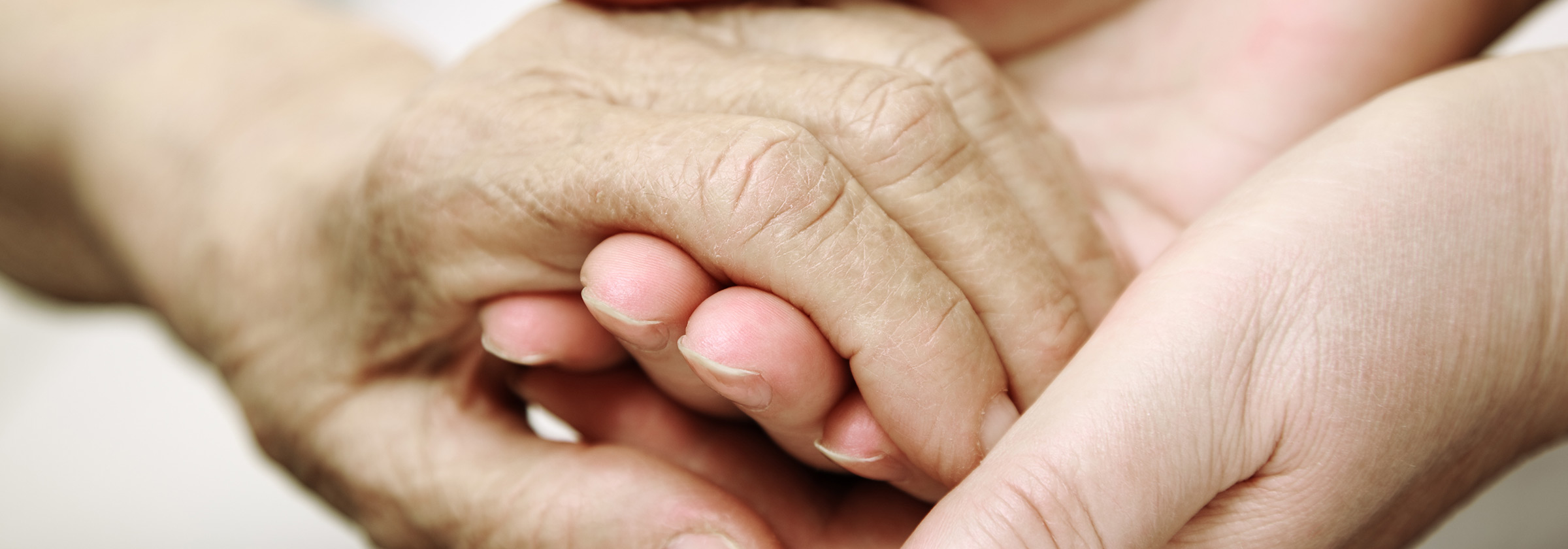 Close up of a young person's hands holding an old person'd hand in their's