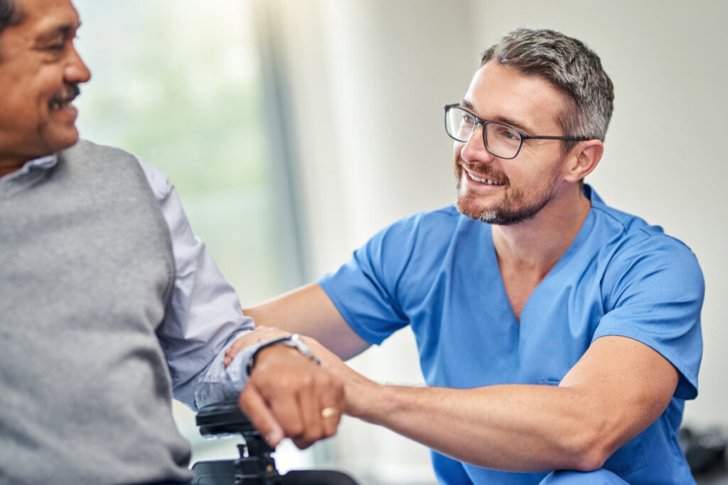 Male nurse smiling and patting the arm of a memory care resident at Traditions of Mount Vernon in Mount Vernon, OH.